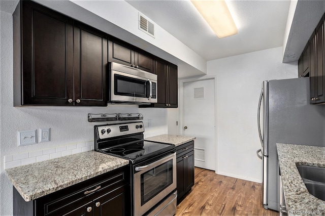 kitchen featuring dark brown cabinetry, light stone counters, light hardwood / wood-style floors, and appliances with stainless steel finishes