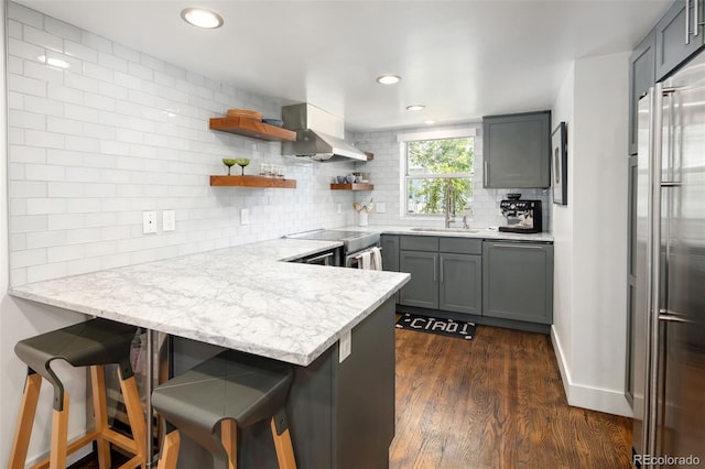 505 Detroit St, Denver, CO 80206 - kitchen with wall chimney range hood, a peninsula, stainless steel built in refrigerator, decorative backsplash, and dark wood-style flooring
