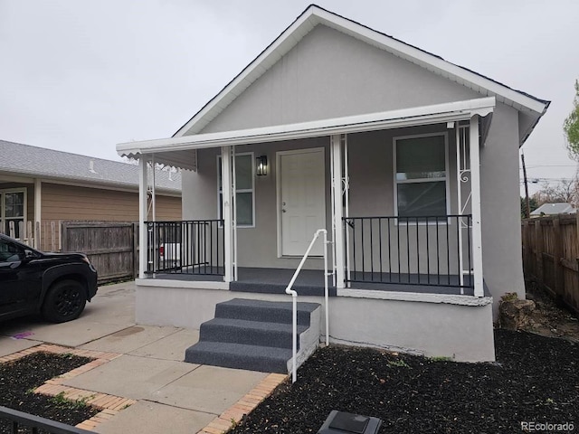 view of front of property with covered porch, fence, and stucco siding