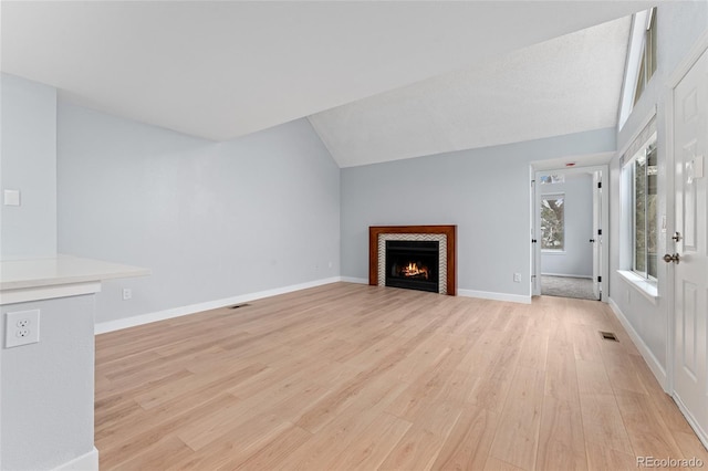 unfurnished living room with light wood-type flooring, lofted ceiling, and a tile fireplace