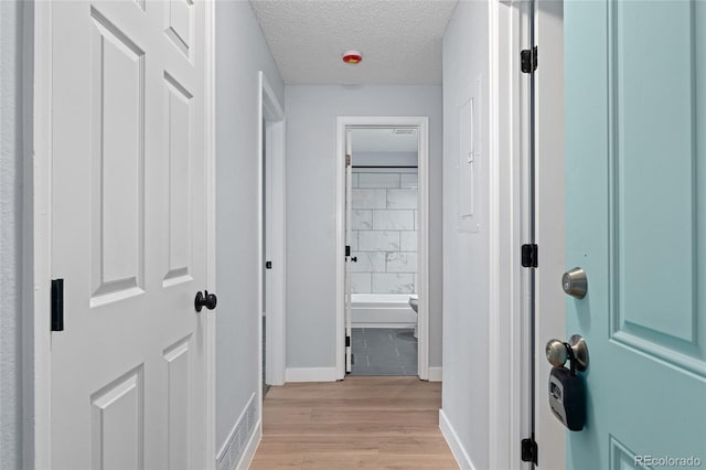 hall with a textured ceiling and light hardwood / wood-style floors