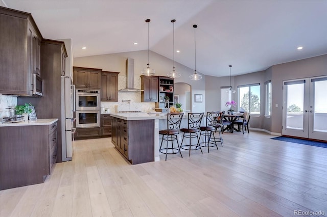 kitchen featuring a kitchen island, decorative light fixtures, backsplash, a kitchen bar, and wall chimney range hood