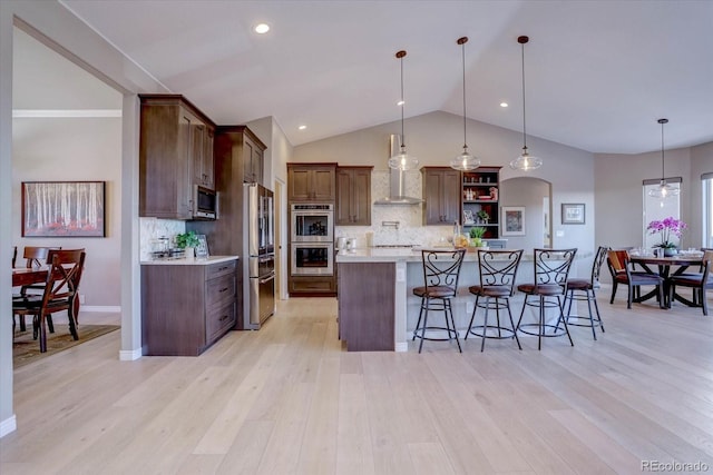 kitchen with appliances with stainless steel finishes, hanging light fixtures, a kitchen breakfast bar, decorative backsplash, and light wood-type flooring