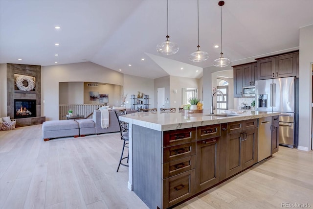 kitchen featuring sink, high end fridge, hanging light fixtures, light hardwood / wood-style floors, and a center island with sink