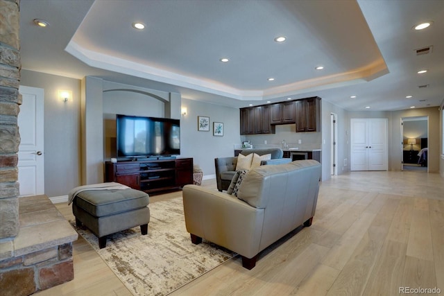 living room featuring sink, light hardwood / wood-style floors, and a raised ceiling