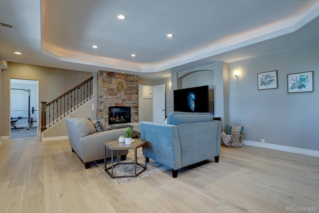 living room with a fireplace, a raised ceiling, and light hardwood / wood-style floors