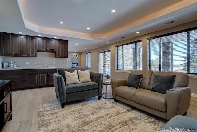 living room featuring indoor wet bar, a tray ceiling, and light hardwood / wood-style flooring