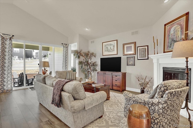 living room featuring baseboards, visible vents, vaulted ceiling, light wood-type flooring, and a fireplace