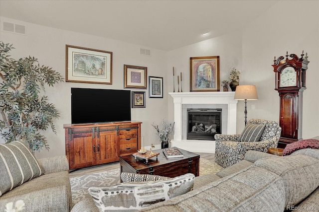 living room featuring lofted ceiling, visible vents, a fireplace, and wood finished floors