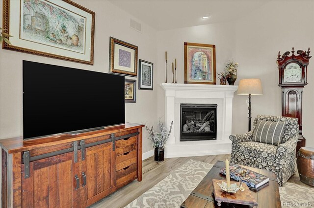 living area featuring lofted ceiling, wood finished floors, visible vents, baseboards, and a glass covered fireplace