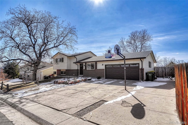 split level home featuring brick siding, a chimney, concrete driveway, an attached garage, and fence