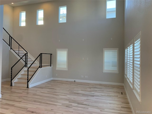 unfurnished living room with a wealth of natural light, light wood-type flooring, and a high ceiling