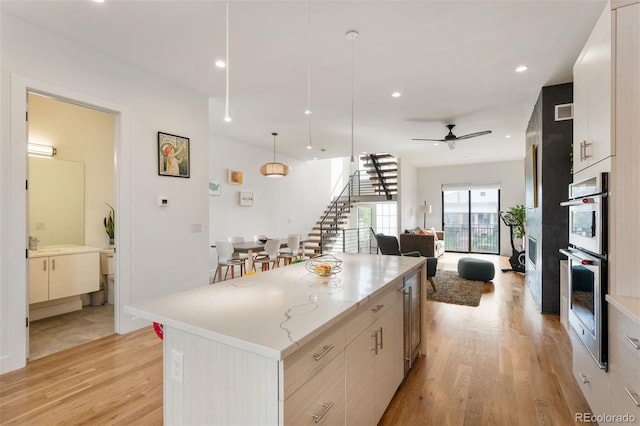 kitchen featuring a ceiling fan, open floor plan, a center island, light wood finished floors, and decorative light fixtures