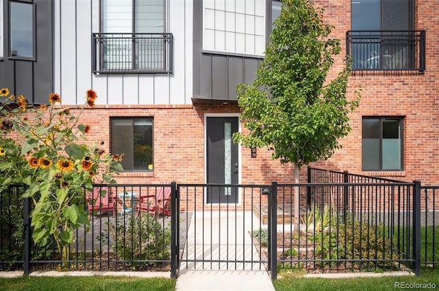 doorway to property featuring board and batten siding, brick siding, and fence