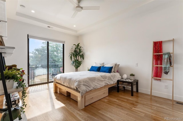 bedroom with access to exterior, visible vents, a raised ceiling, and light wood finished floors