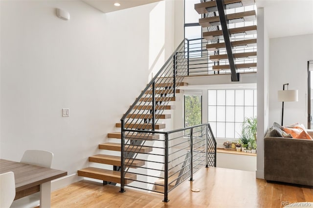 staircase with wood finished floors, a towering ceiling, and baseboards