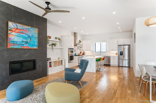 living area featuring recessed lighting, a fireplace, light wood finished floors, and ceiling fan