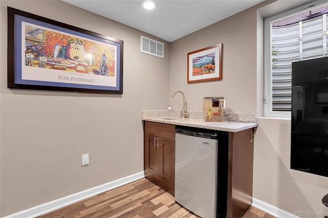 bar featuring stainless steel refrigerator, dark brown cabinetry, sink, and light hardwood / wood-style flooring