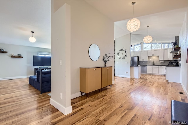 living room featuring sink, light wood-type flooring, lofted ceiling, and an inviting chandelier