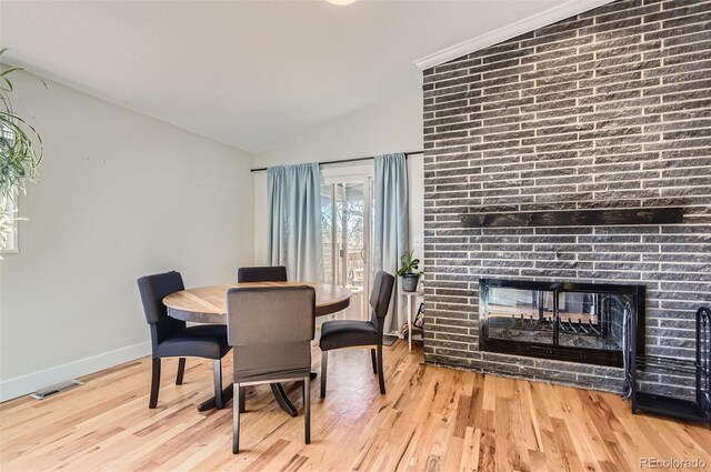 dining area featuring a multi sided fireplace, light hardwood / wood-style flooring, and vaulted ceiling