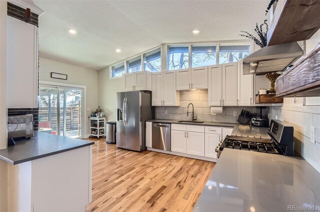 kitchen with vaulted ceiling, sink, white cabinetry, appliances with stainless steel finishes, and a textured ceiling