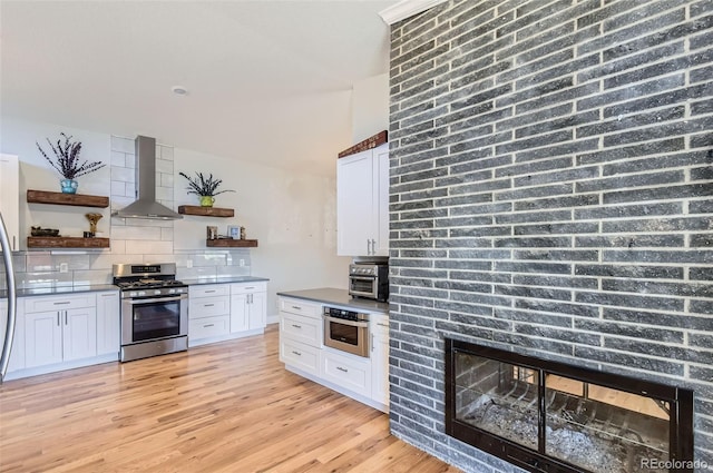 kitchen featuring wall chimney range hood, white cabinets, decorative backsplash, and stainless steel range with gas stovetop