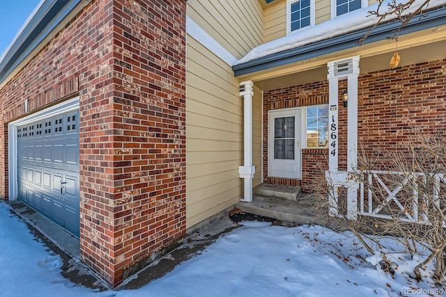 snow covered property entrance featuring a garage