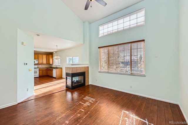 unfurnished living room with high vaulted ceiling, sink, ceiling fan, light hardwood / wood-style floors, and a tiled fireplace