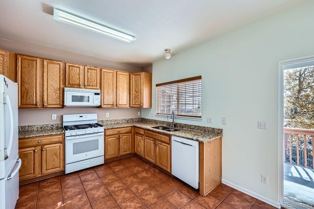 kitchen with dark tile patterned flooring, a healthy amount of sunlight, white appliances, and sink