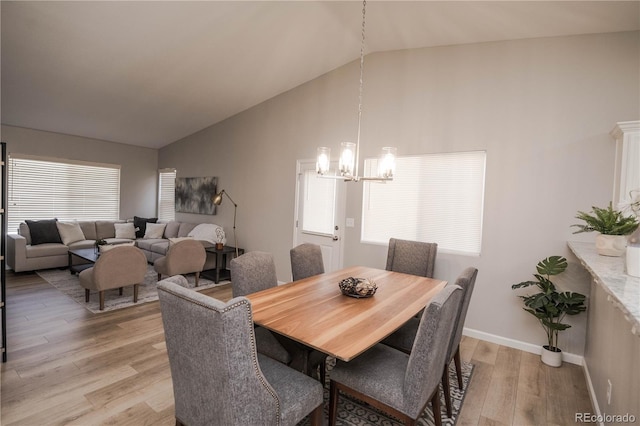 dining space with light wood-style floors, baseboards, high vaulted ceiling, and an inviting chandelier