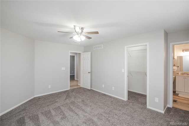 unfurnished bedroom with carpet, a walk in closet, visible vents, and baseboards