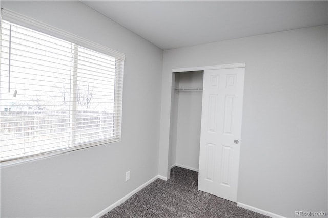 unfurnished bedroom featuring baseboards, dark colored carpet, and a closet