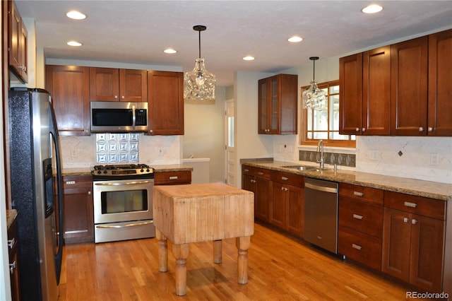 kitchen with appliances with stainless steel finishes, light stone counters, hanging light fixtures, and sink