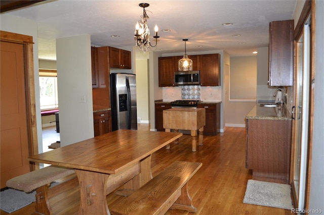 interior space with backsplash, sink, hanging light fixtures, light hardwood / wood-style flooring, and stainless steel appliances