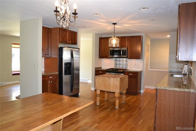 kitchen featuring stainless steel appliances, sink, decorative light fixtures, hardwood / wood-style flooring, and a notable chandelier