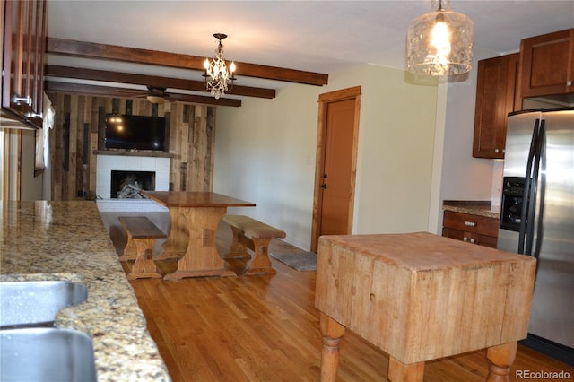 kitchen with a center island, a fireplace, beamed ceiling, light stone counters, and stainless steel fridge with ice dispenser