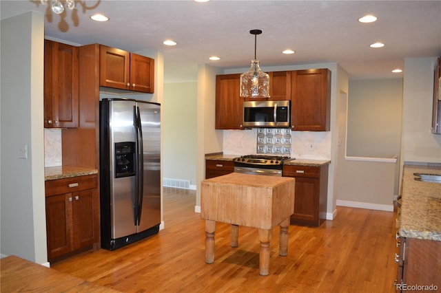 kitchen with light stone countertops, stainless steel appliances, tasteful backsplash, decorative light fixtures, and light wood-type flooring