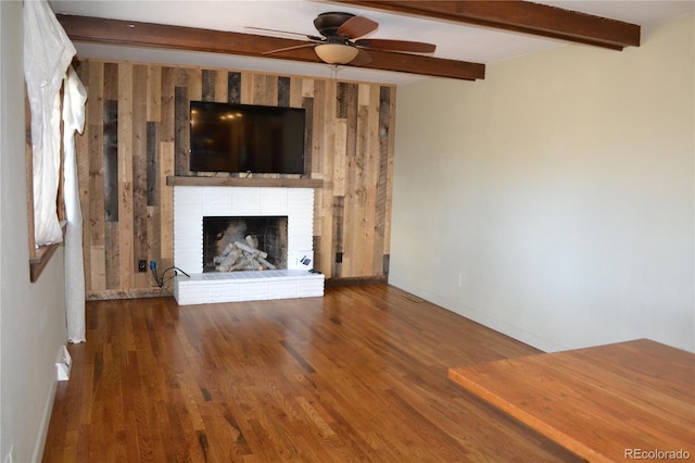 unfurnished living room featuring beam ceiling, ceiling fan, a fireplace, and wood-type flooring