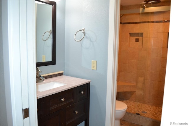 bathroom with a tile shower, vanity, and toilet