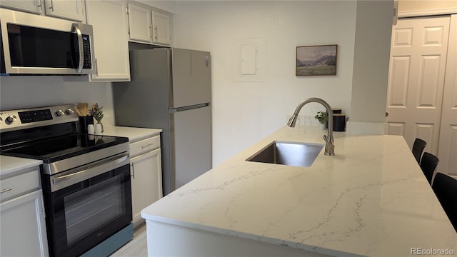 13854 E Lehigh Ave Unit D, Aurora, CO 80014 - kitchen featuring appliances with stainless steel finishes, a sink, light stone counters, light wood-type flooring, and white cabinets
