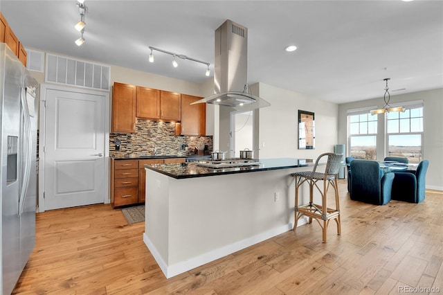 13598 Via Varra Unit 301, Broomfield, CO 80020 - kitchen with island range hood, stainless steel appliances, brown cabinets, backsplash, and light wood-style flooring
