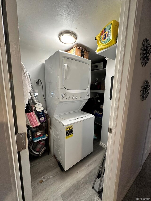 laundry room with stacked washer and dryer, a textured ceiling, and light wood-type flooring