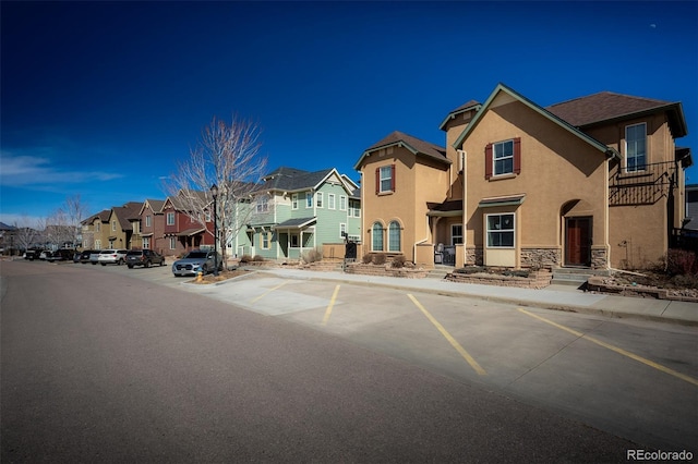 view of front of property featuring uncovered parking, a residential view, stone siding, and stucco siding