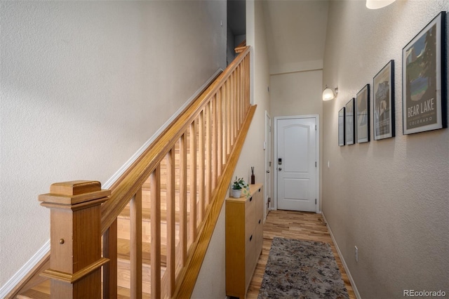 hallway featuring a textured wall, stairway, a high ceiling, wood finished floors, and baseboards