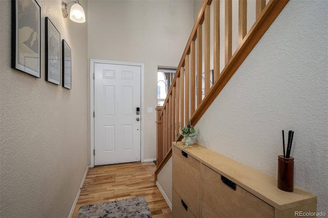 entryway with light wood finished floors, stairs, baseboards, and a textured wall