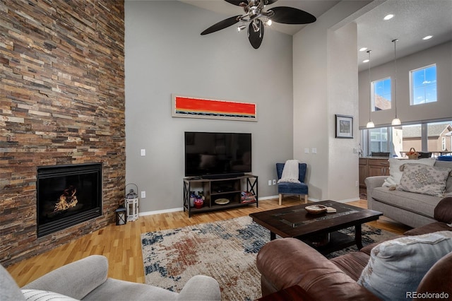 living room with a high ceiling, a fireplace, wood finished floors, and baseboards