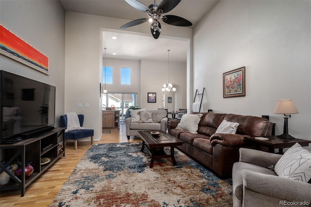 living area featuring a towering ceiling, light wood finished floors, and ceiling fan with notable chandelier