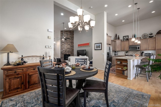 dining space featuring ceiling fan with notable chandelier, a high ceiling, light wood-type flooring, and a fireplace