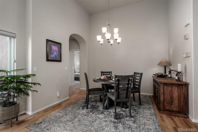 dining space featuring baseboards, visible vents, arched walkways, wood finished floors, and a notable chandelier