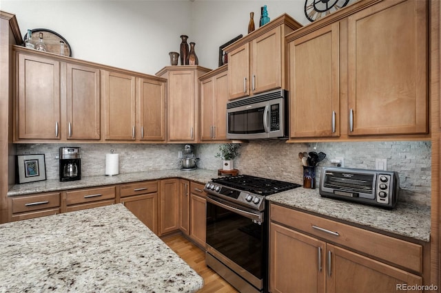 kitchen with appliances with stainless steel finishes, light wood-style flooring, decorative backsplash, and light stone countertops